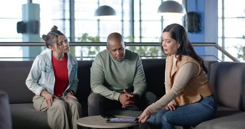 Diverse team collaborating in modern office lounge discussing tablet and ideas