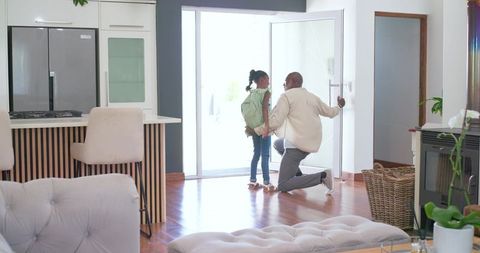 African american father kneeling adjusting daughter's backpack before school