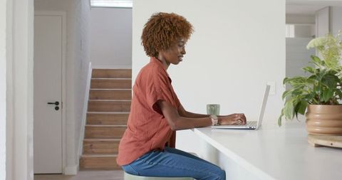 African american woman working on laptop at bright kitchen counter, remote work focus