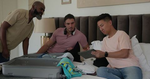 Friends packing for wedding getaway in stylish hotel room