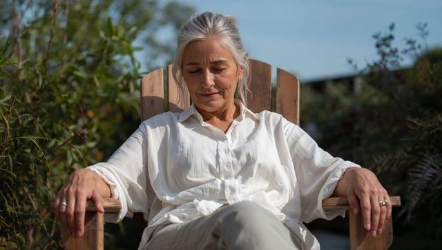 Silver-haired woman relaxing in adirondack chair on garden terrace wearing white shirt