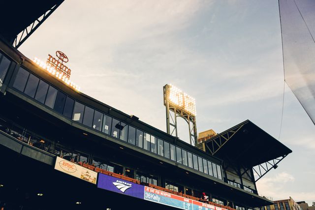 Outdoor baseball stadium during sunset with illuminated stadium lights and an electronic scoreboard. Can be used for topics related to sports events, baseball games, architectural design of sports venues, and evening sports activities.