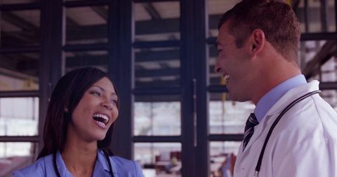 Laughing medical team members collaborating in clinic corridor with stethoscopes