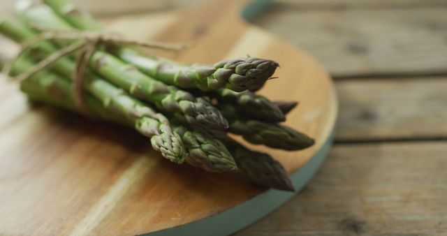 Fresh bunch of green asparagus tied with string resting on wooden cutting board. Ideal for food blogs, nutrition websites, healthy eating promotions, and cookbook illustrations.