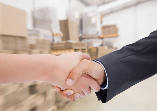 Business executives shaking hands in a warehouse, symbolizing successful partnership and collaboration. Ideal for use in articles and advertisements related to business agreements, logistics, supply chain management, and corporate success.