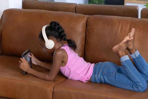 African american girl listening with headphones using tablet on brown sofa