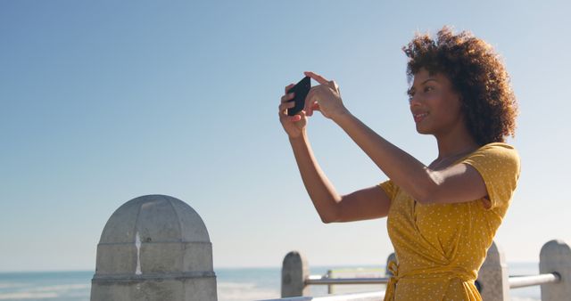 Woman in Yellow Dress Taking Selfie on Sunny Seaside Promenade - Download Free Stock Images Pikwizard.com