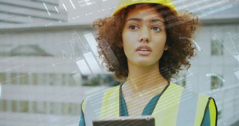 Image depicts professional female architect with curly hair wearing a yellow hard hat and vest, working on a construction site with a focus on a digital tablet displaying various statistics. Useful for illustrating concepts of modern architecture, engineering, productivity, tech use in construction management, and women's roles in industry.