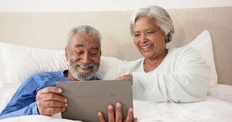 Senior Couple Relaxing in Bed Using Tablet for Entertainment