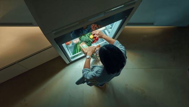 Woman reaching into built-in fridge grabbing fresh produce in modern kitchen