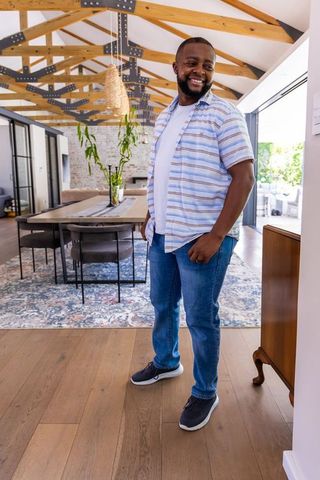Smiling african american man standing in modern open-plan dining room with timber beams