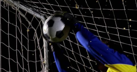Diving goalkeeper catching ball in goal during night match dramatic save action
