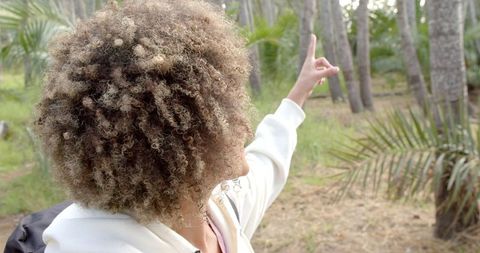 Happy Woman with Curly Hair Enjoying Nature Outdoors, Pointing Upwards