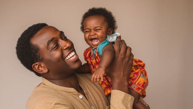 Father laughing while holding joyful baby in warm studio portrait, parenthood bond family love