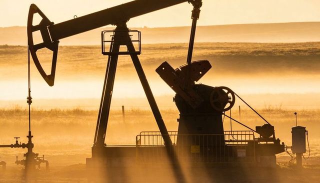 Golden sunrise pump jack silhouette pumping over foggy prairie with walking beam and piping
