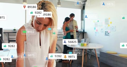 Blonde woman writing at desk with floating social media notifications, team collaboration
