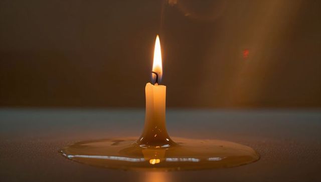 Solitary burning candle with melted wax pooling