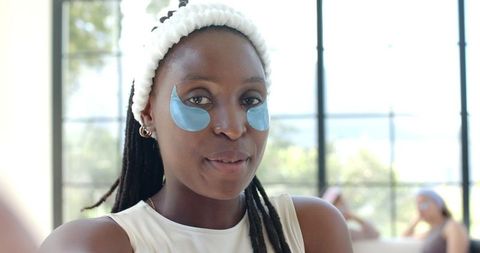 Woman wearing white headband and blue hydrogel eye patches enjoying spa skincare glow