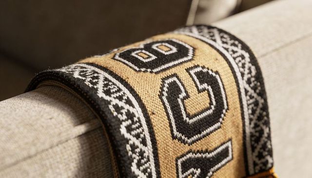 Draping knitted throw with bold numeric motifs over beige sofa armrest for cozy home styling