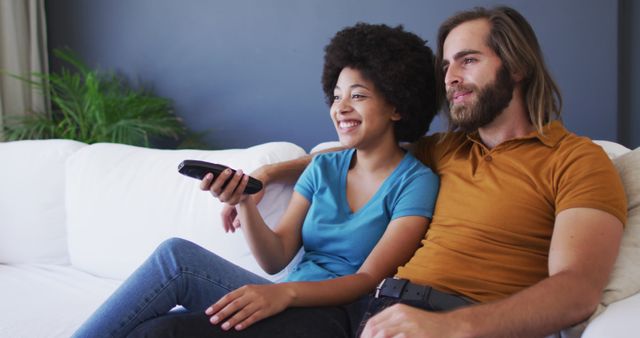 Biracial couple watching tv together while sitting on the couch at home - Download Free Stock Photos Pikwizard.com