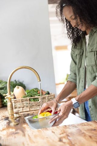 Washing bell peppers under brass faucet in rustic kitchen for healthy home cooking