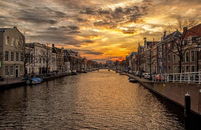 Sunset over tranquil canal lined with historic buildings reflecting in the water in Amsterdam. Idyllic scene with warm colors and calm water. Great for travel blogs, tourism promotions, postcards, and inspiring wanderlust.