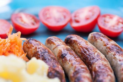 Sizzling bratwurst sausages with creamy mashed potato and halved cherry tomatoes on plate