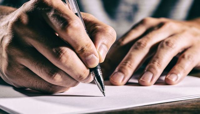 Closeup Male Hands Writing with Retractable Ballpoint on White Paper over Wooden Desk