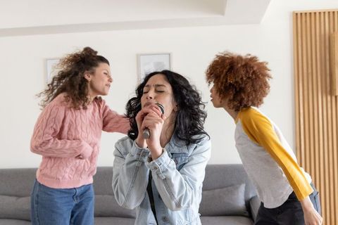 Diverse friends singing karaoke in living room, woman holding microphone leading casual jam session