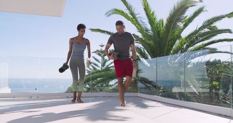 Diverse Couple Holding Yoga Mats on Ocean View Balcony