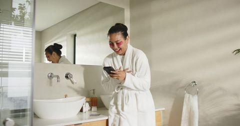 Mid-adult asian woman enjoying at-home spa routine with eye patches and smartphone