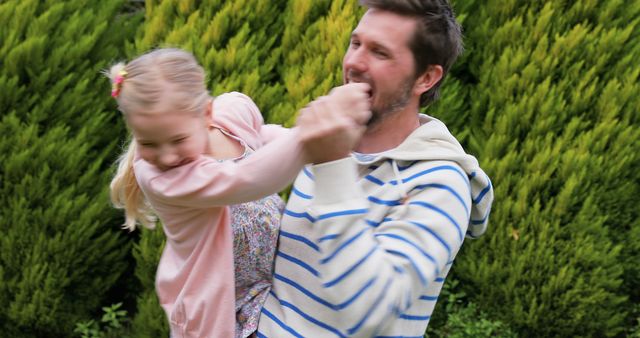 Happy caucasian father and daughter dancing in garden. Fatherhood, childhood, togetherness, nature and lifestyle, unaltered.