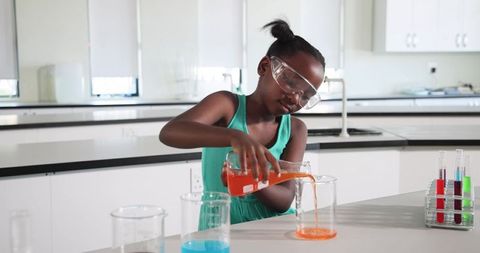 African american girl conducting colorful chemistry experiment in school lab with beakers