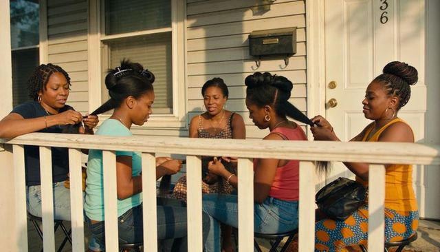 Women braiding hair on sunny porch, friends and family sharing stories while styling