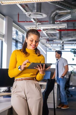 Young professional woman using tablet and smiling in bright modern open-plan office space