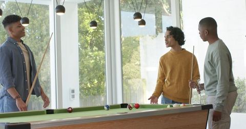 Young Men Playing Pool and Chatting in Bright Modern Game Room with Large Windows