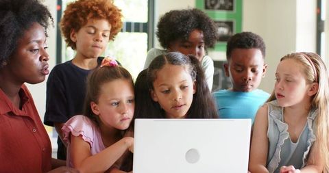 African American Teacher Guiding Multiracial Children Collaborating Around Laptop