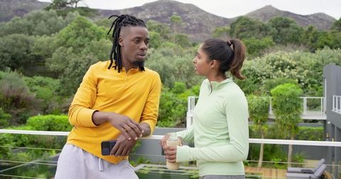 African American man and Indian woman chatting on modern terrace overlooking lush garden