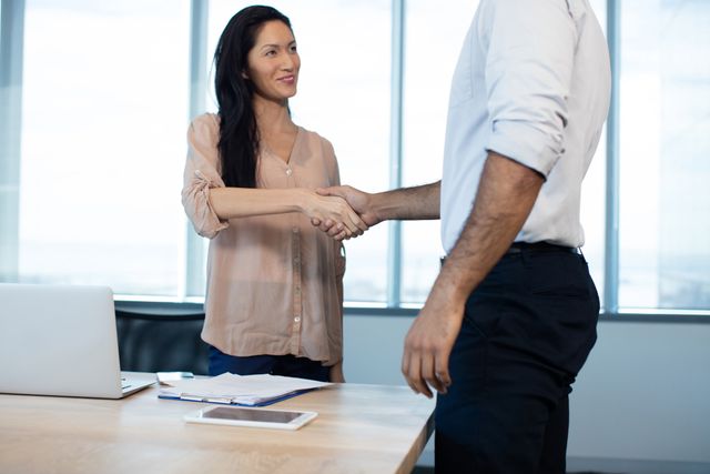 Business professionals shaking hands in an office conference room, symbolizing agreement and partnership. Ideal for use in articles or advertisements related to business deals, professional collaboration, corporate success, and teamwork.