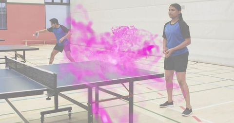 Returning player delivering serve at table tennis with magenta powder burst, indoor gym action