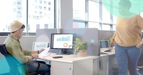 Analyzing printed and digital charts at modern open office desk with coworker collaboration