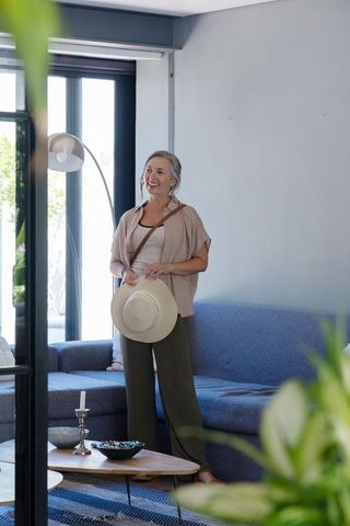 Senior woman preparing for day out in sunlit modern living room holding straw hat