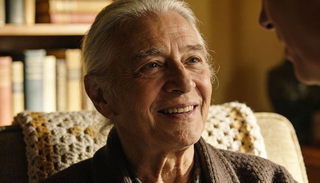 Smiling senior woman looking at companion in cozy home with crochet blanket and bookshelf