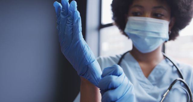 Healthcare worker in medical scrubs and mask putting on nitrile gloves, representing readiness and attention to safety in a hospital or medical environment. This image is ideal for depicting professional healthcare services, safety protocols, and medical practices in hospitals and clinics. Useful for healthcare articles, medical blogs, or promotional material for healthcare facilities.