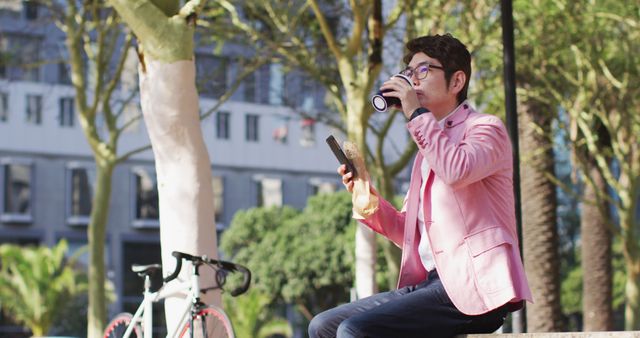 Asian man drinking coffee and using smartphone while sitting at the park. business and lifestyle concept