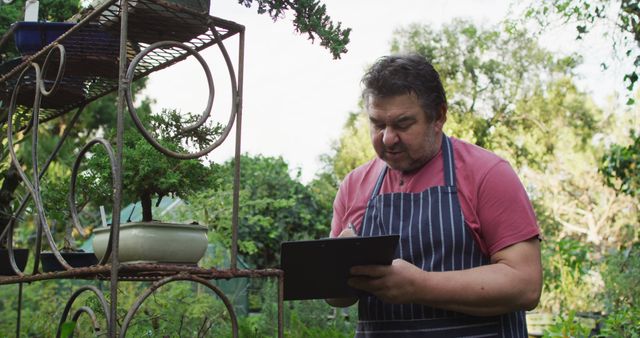 Middle-aged man tending garden with clipboard on sunny day - Download Free Stock Images Pikwizard.com