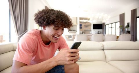 Smiling Man Relaxing on Couch Using Smartphone in Modern Living Room