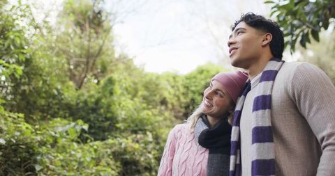 Cozy couple gazing upward in woodland wearing knit sweaters and scarves, autumn outdoors