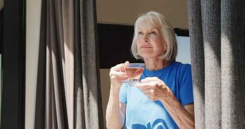 Senior woman enjoying tea by window with contemplative gaze