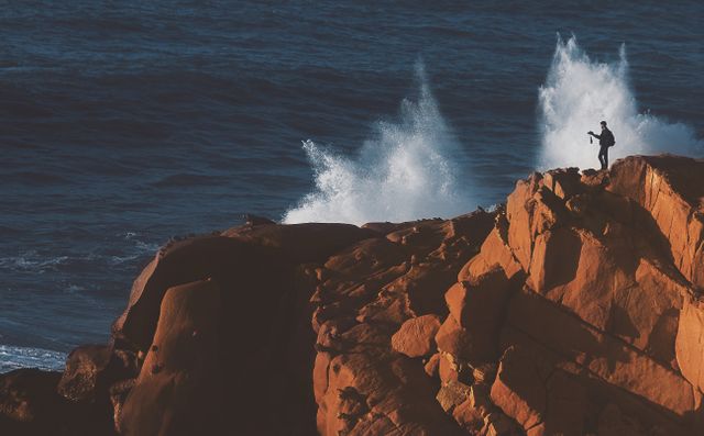 Shows a fisherman casting a line from a rugged rocky cliff with waves crashing in the background. Captures the essence of adventure and the power of nature. Perfect for use in travel blogs, outdoor adventure promotions, and fishing-related content.